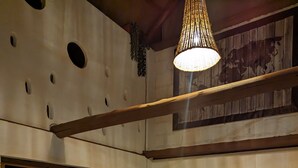 Een eethoek met een tafel gedekt voor twee personen, houten stoelen, een hanglamp en een uitzicht op de aangrenzende kamer.