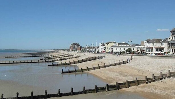 Een kustgebied met een zandstrand, een houten steiger en gebouwen langs de boulevard.