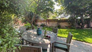 Een ronde houten tafel met zes stoelen, een fles wijn en een bord met fruit.