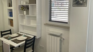 A dining area with a white table set for two, a white radiator below, and a window with blinds. - Little Aventino BnB - in the heart of Rome (Roma)