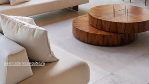Una sala de estar moderna con un sofá blanco, una mesa de centro de madera y vistas a un exuberante paisaje exterior.