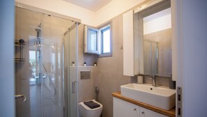 A modern bathroom with a glass shower enclosure, a toilet, a sink with a wooden countertop, and a mirror above the sink. - Whisper Villa Mykonos (Mykonos)