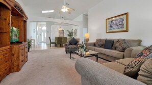 A spacious living room with a wooden cabinet, a sofa set, a coffee table, and a ceiling fan. - Affordable 5BR Disney Villa with Pool, Spa & Game Room - Indian Creek Community (Kissimmee)