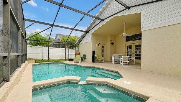 A swimming pool with a glass enclosure, a covered patio with chairs, and a view of the backyard. - Affordable 5BR Disney Villa with Pool, Spa & Game Room - Indian Creek Community (Kissimmee)