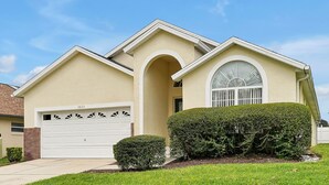 A single-story house with a garage, a large arched window, and a well-maintained lawn. - Affordable 5BR Disney Villa with Pool, Spa & Game Room - Indian Creek Community (Kissimmee)