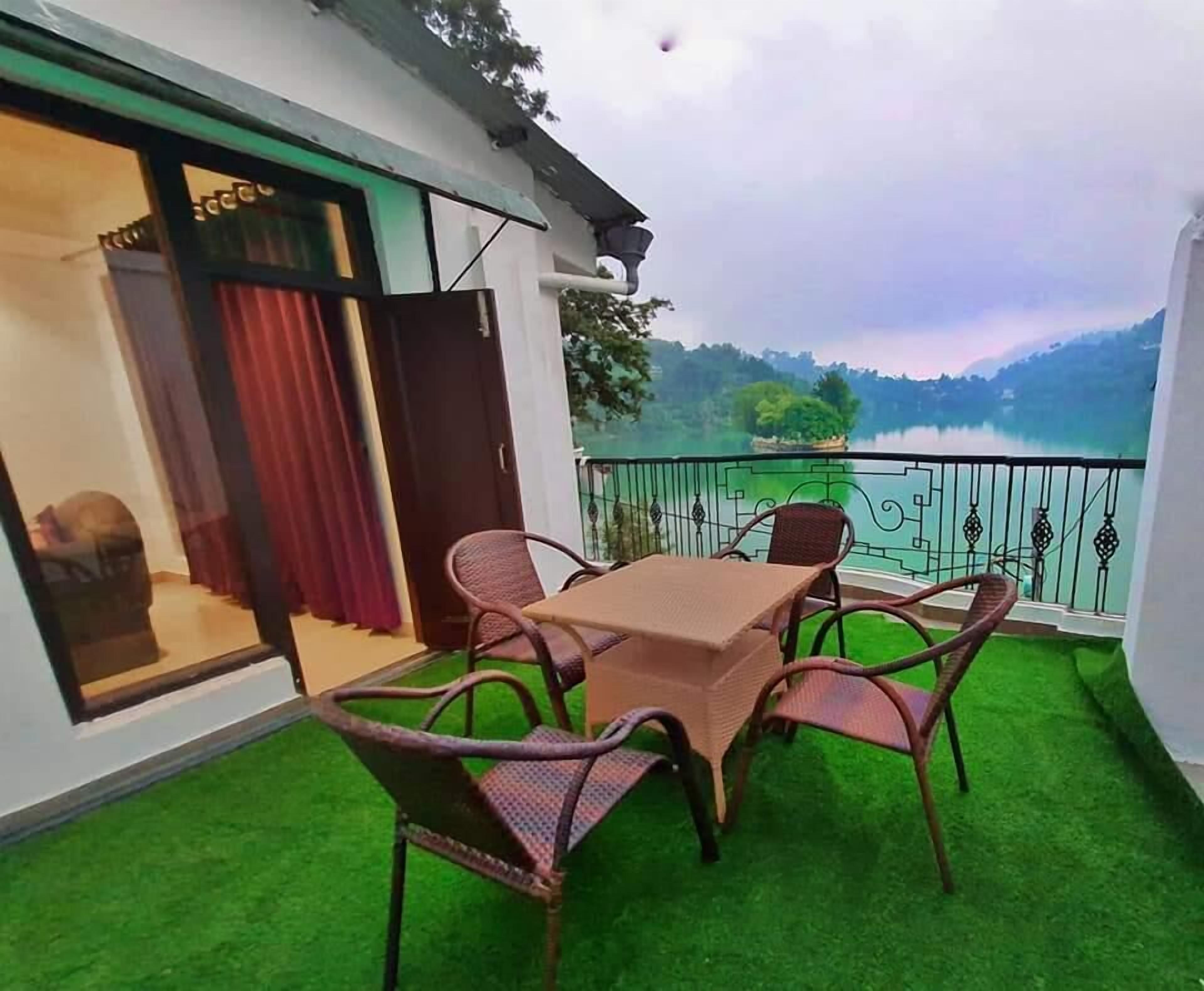 A balcony with a table and chairs, a view of a lake, and a green lawn.
