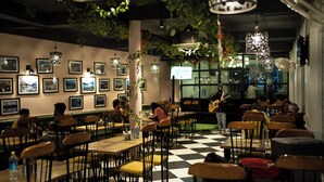 A restaurant with a checkered floor, wooden chairs, and tables. There are framed pictures on the walls and hanging lights. - The Lake Heritage @Bhimtal Lake (Nainital)