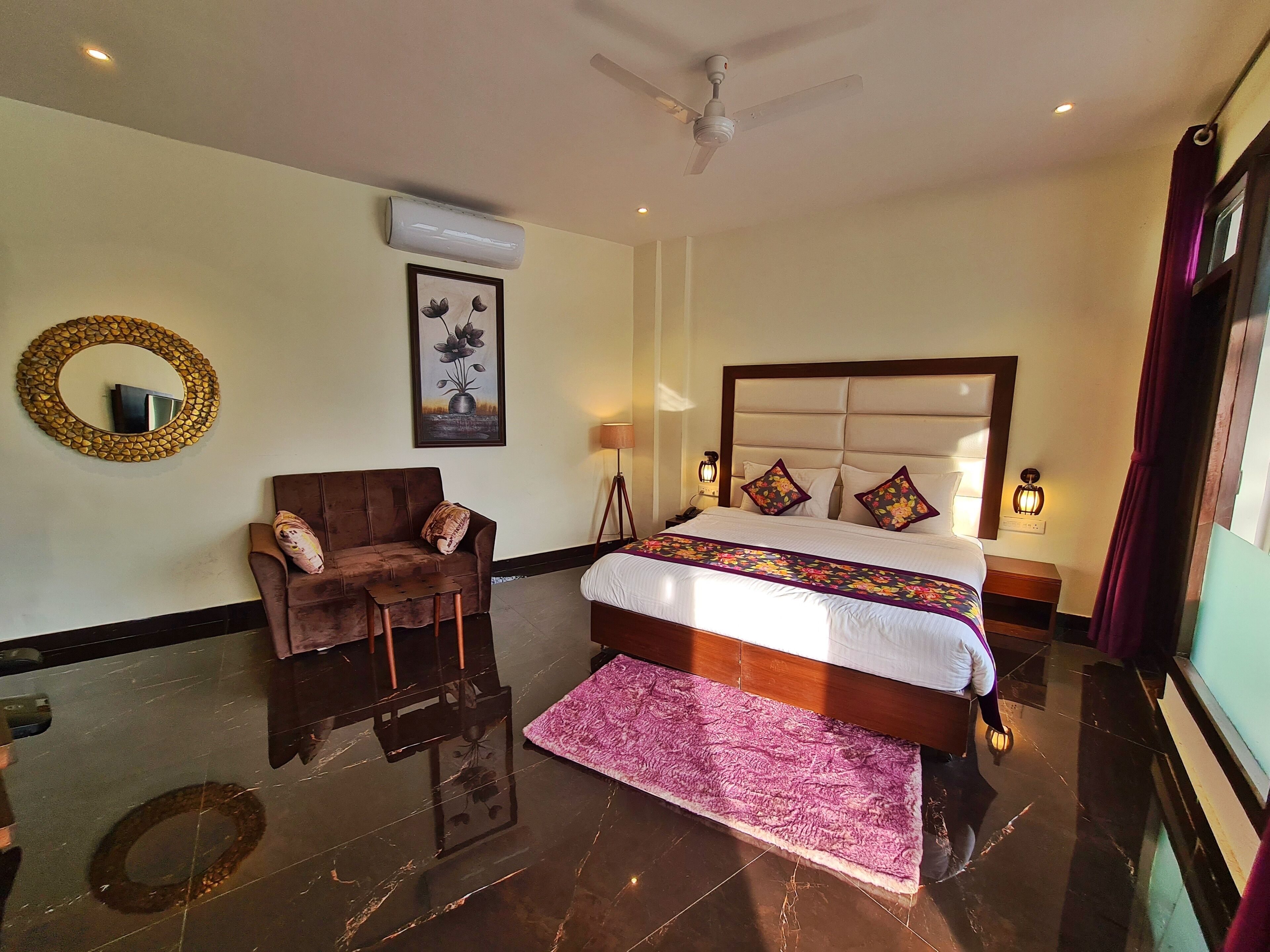 A hotel room with a bed, a chair, a round mirror, a framed picture, and a standing lamp.