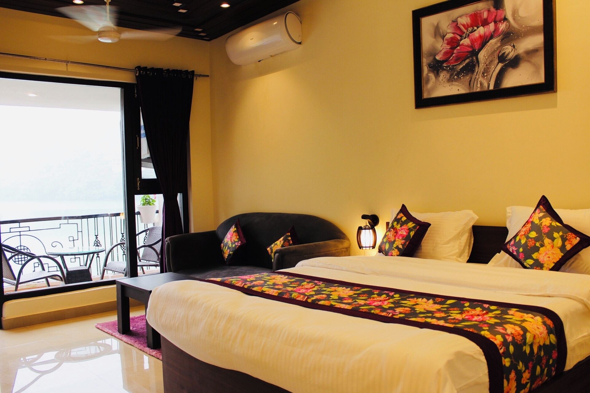 A hotel room with a bed, a chair, a table, and a balcony with outdoor furniture.