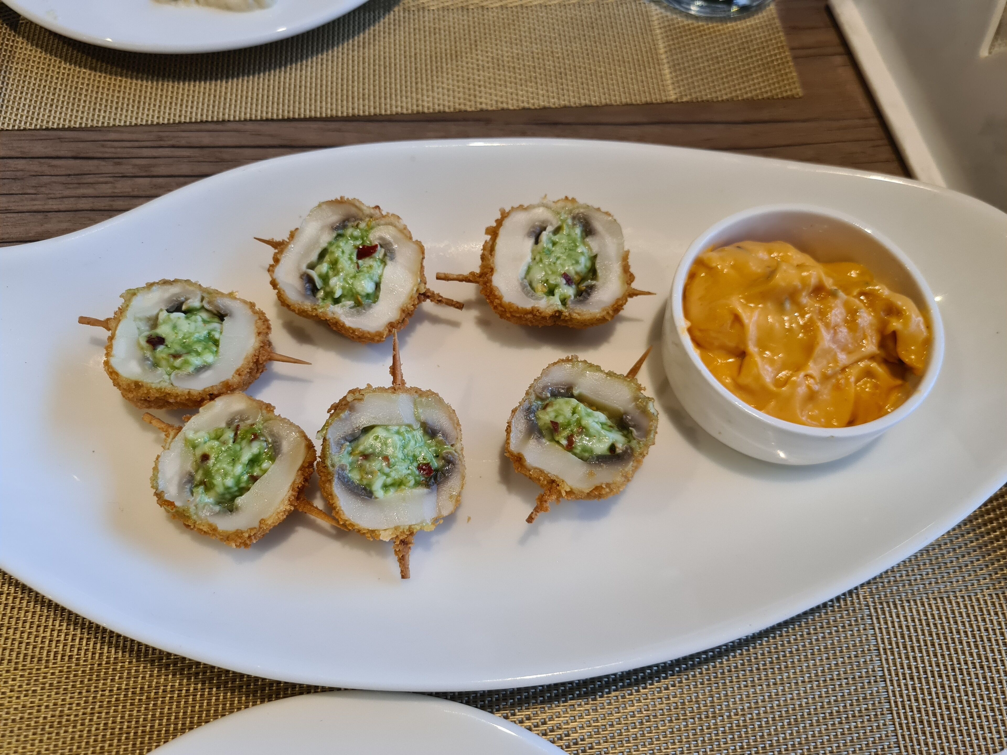 Un plato blanco con seis champiñones rellenos y un cuenco de salsa naranja.