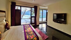 A bedroom with a bed, a TV, a ceiling fan, and a view of a body of water through large windows. - The Lake Heritage @Bhimtal Lake (Nainital)