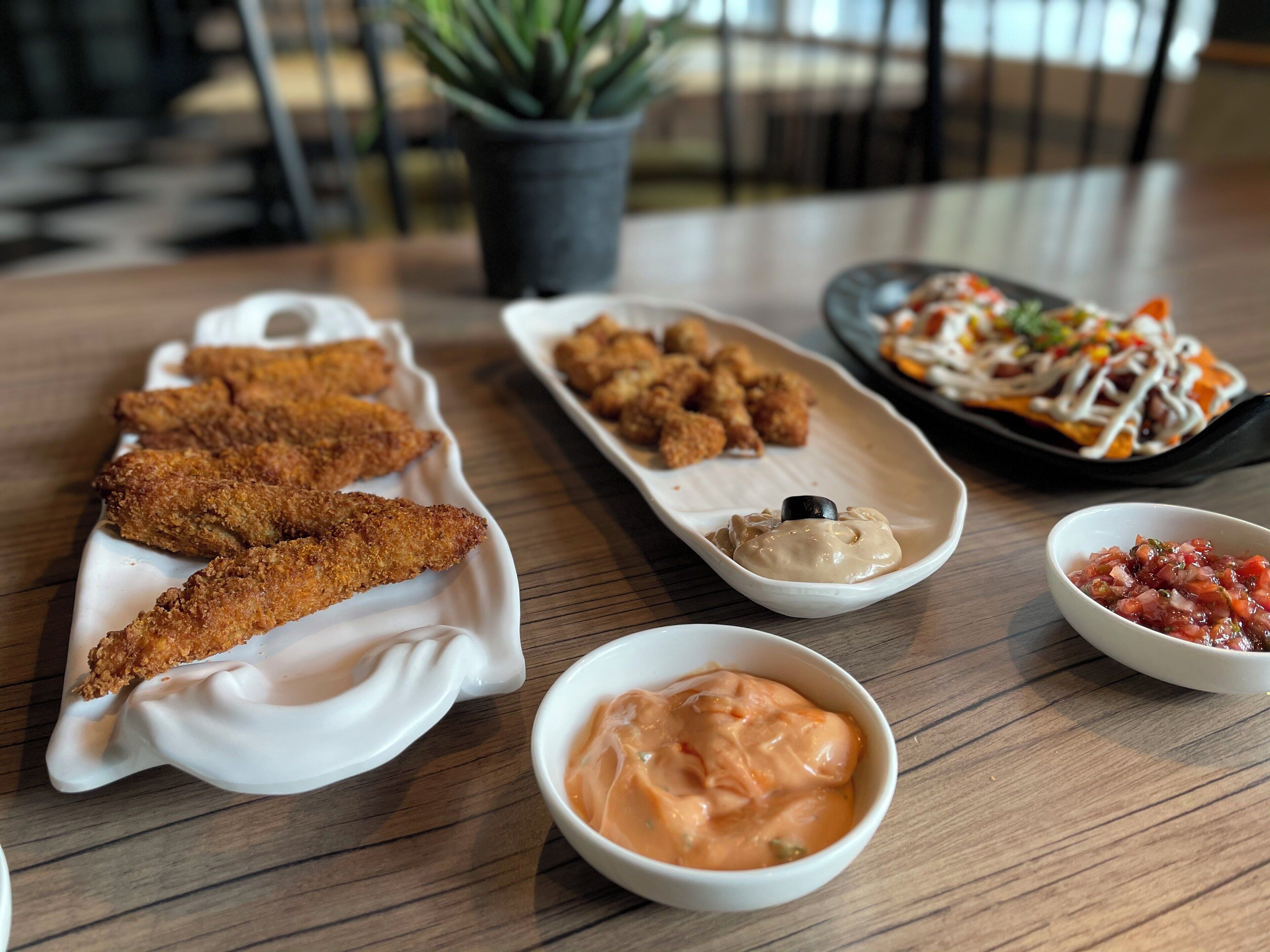 A table with various dishes including breaded items, a bowl of sauce, and a plate with a salad.