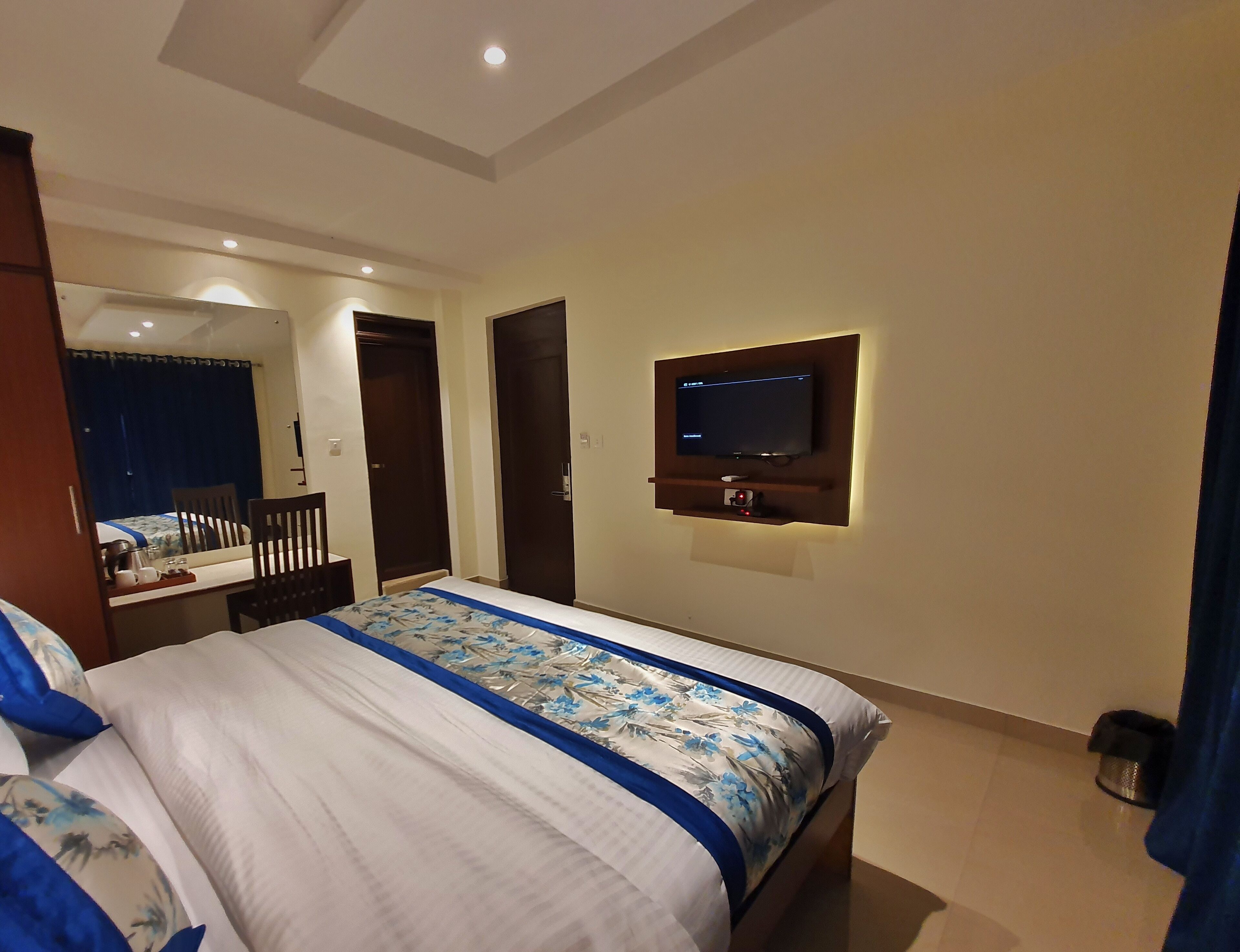 A hotel room with a bed, a TV mounted on the wall, a desk with a chair, and a mirror.