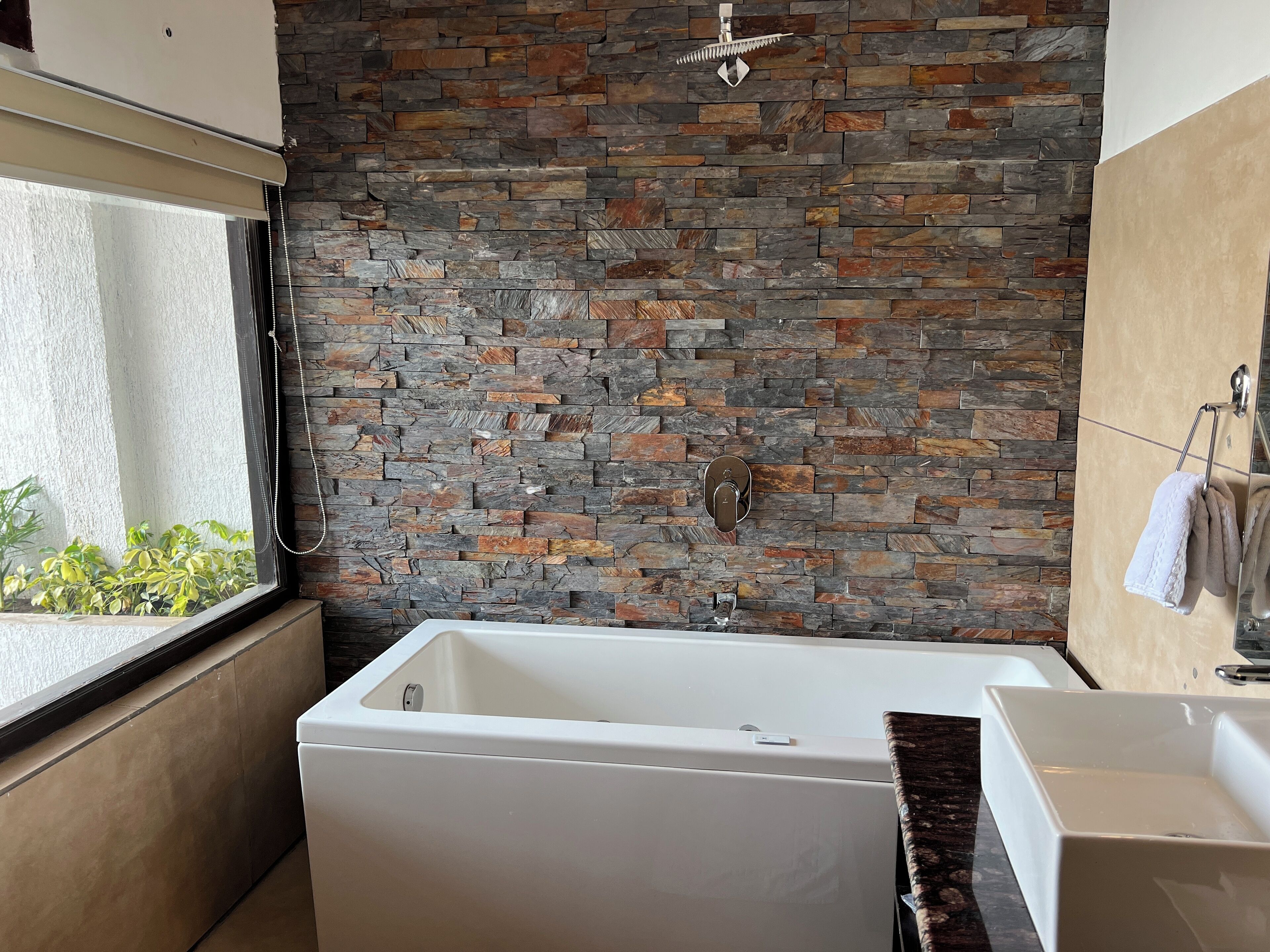A modern bathroom with a stone wall, a bathtub, and a sink.