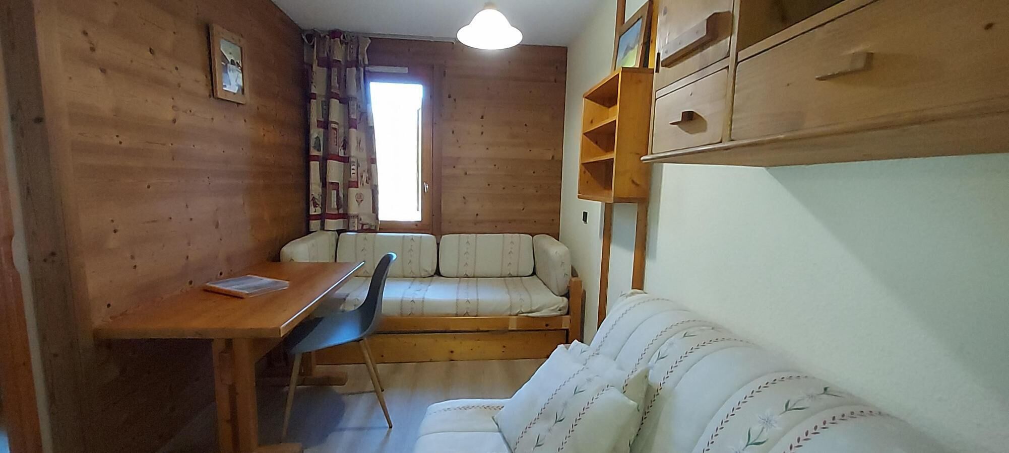 A compact room with a wooden interior, a sofa, a small table, and a window with curtains.