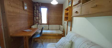 A compact room with a wooden interior, a sofa, a small table, and a window with curtains.