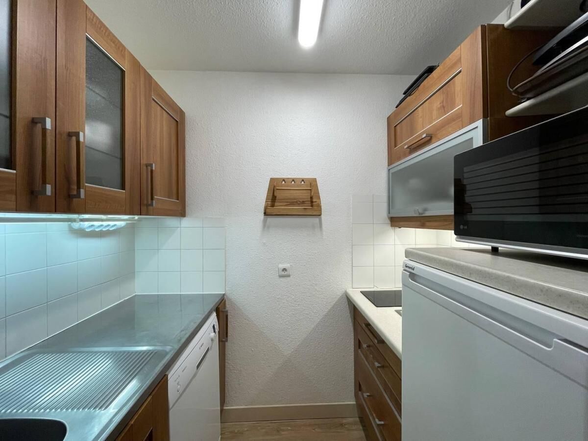 A compact kitchen with wooden cabinets, a stainless steel countertop, a built-in microwave, and a dishwasher.