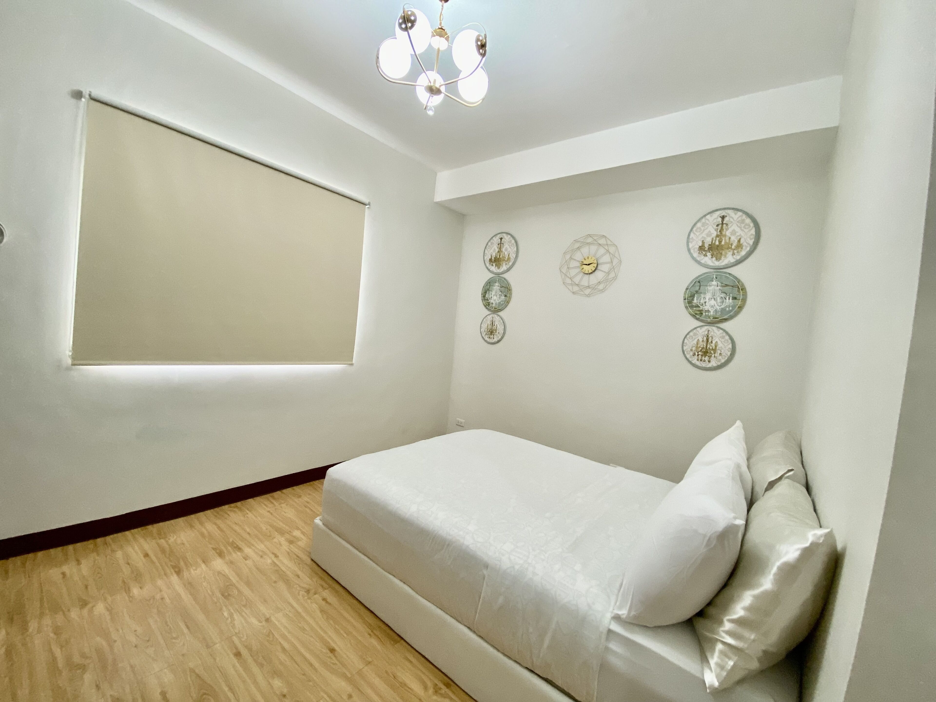 A bedroom with a bed, a window with a blind, and wall decorations.