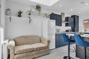 A modern kitchen with dark cabinets, a white refrigerator, and a beige sofa.