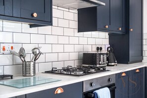 A modern kitchen with black cabinets, a gas stove, and a coffee machine. - Spacious 3BR Home | Garage & Near Birmingham (West Bromwich)