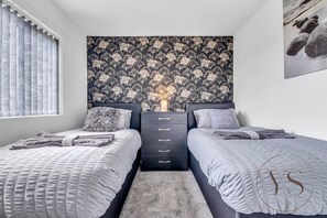 A bedroom with two beds, a dresser, a floral wallpaper, and a painting on the wall. - Spacious 3BR Home | Garage & Near Birmingham (West Bromwich)