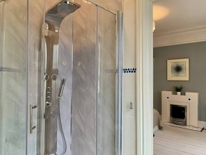 A modern bathroom with a glass-enclosed shower, a marble floor, and a fireplace in the adjacent room. - 6BR Home with Parking Near Wolverhampton (Willenhall)