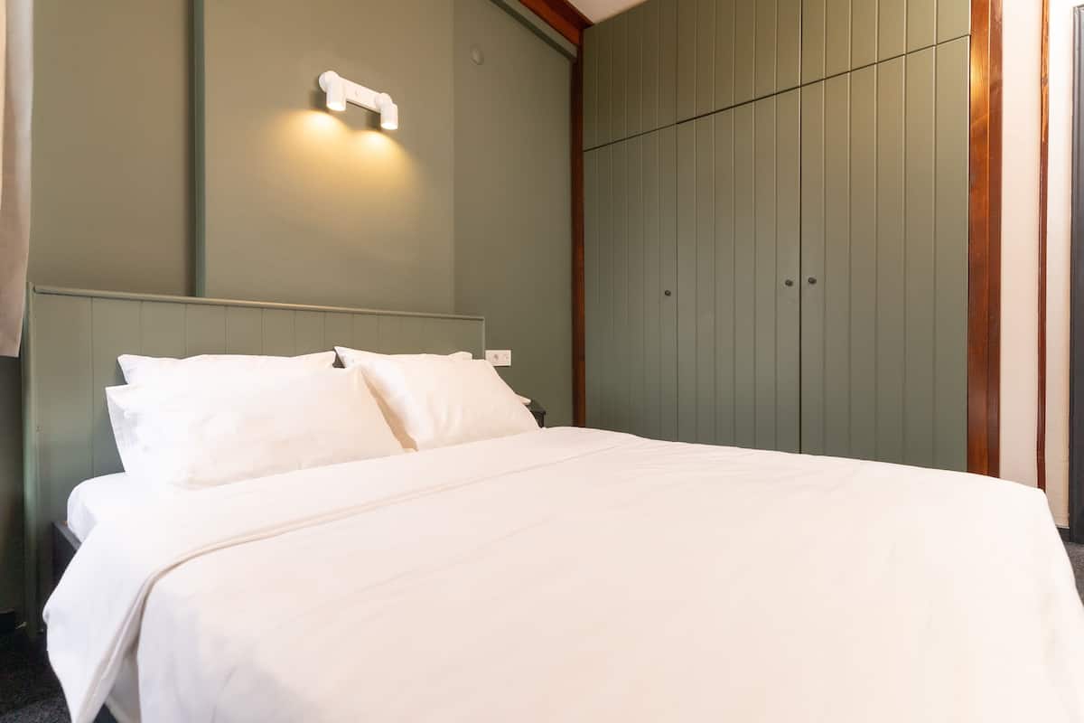 A neatly made bed with white linens in a room with a green wall and wooden paneling.