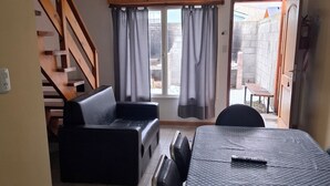 Ein Zimmer mit einem karierten Tisch, einer Couch, einer Treppe und einem Blick durch ein mit Vorhängen drapiertes Fenster.