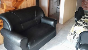 En svart lädersoffa, en trappa i trä och ett köksområde med skåp och en diskho.