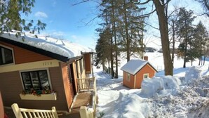 En stuga byggd av trä med en balkong, ett litet uthus som sitter ihop med stugan och en snötäckt stig som leder till entrén.