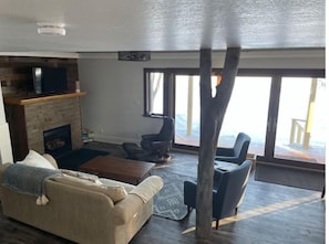 A living room with a fireplace, a sofa, a coffee table, and a large window overlooking a deck.