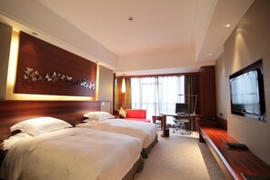 A hotel room with two beds, a desk with a chair, a TV, and a large window with curtains.