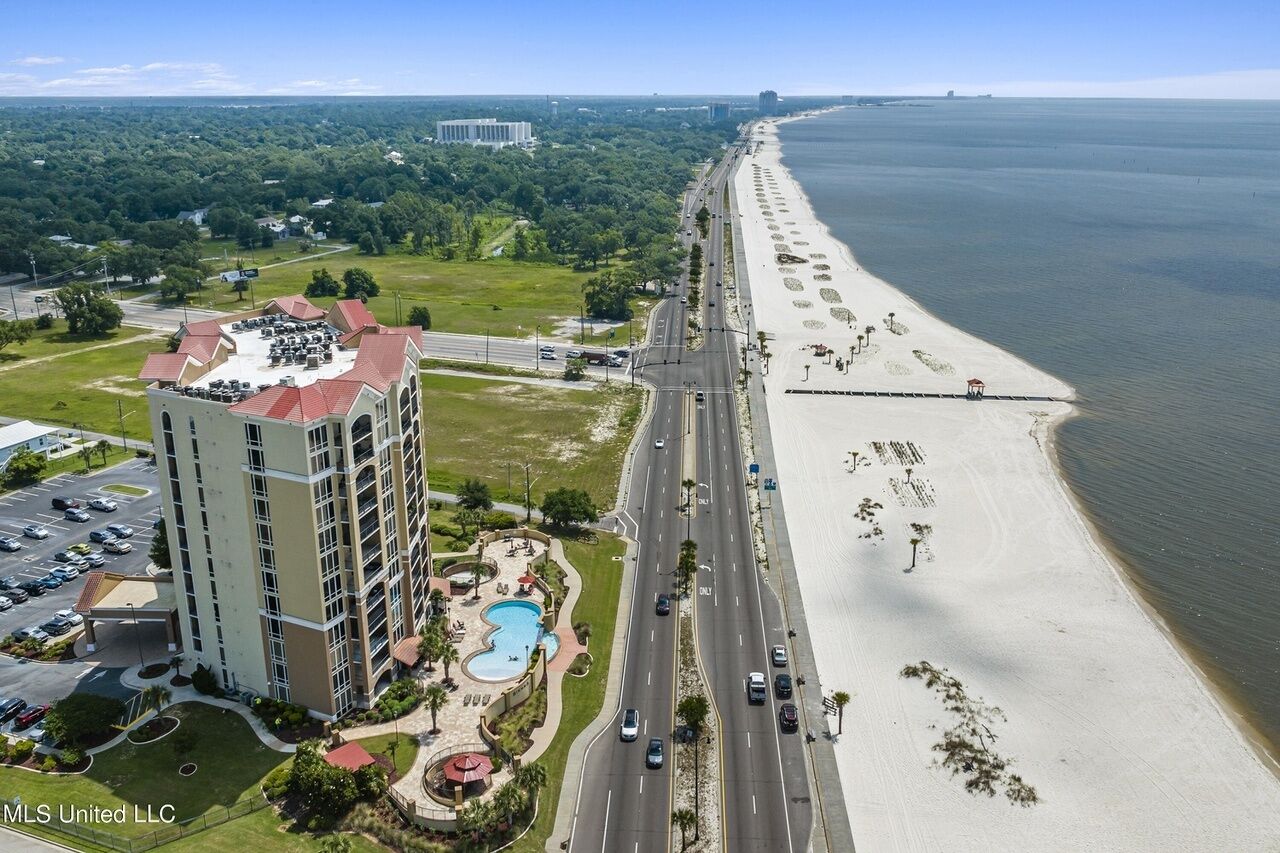 An aerial view of a coastal hotel with a swimming pool, a parking lot, and a beach.