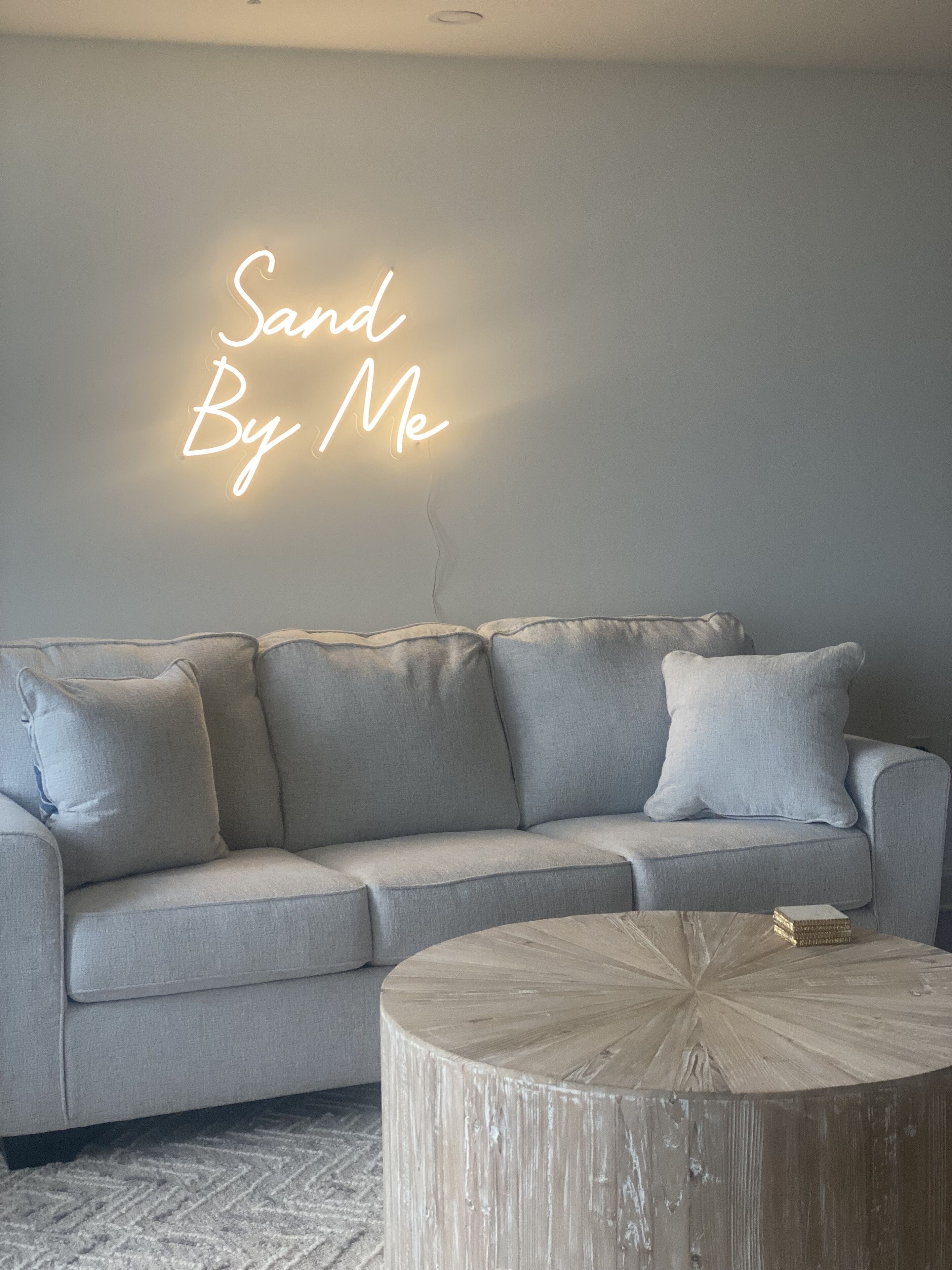 En grå soffa med ett runt soffbord i trä och en neonreklamskylt på väggen.