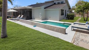A modern house with a swimming pool, a patio with lounge chairs, and a well-maintained lawn.