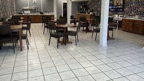 Un restaurant spacieux doté de nombreuses tables et chaises, d’un espace cuisine et d’un grand écran affichant le menu.