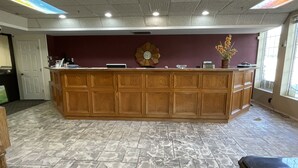 Un espace d’accueil avec un comptoir en bois, une horloge et un vase rempli de fleurs.