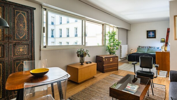 Ein modernes Wohnzimmer mit einem Holzesstisch, einer Couch, einem Couchtisch und einem großen Fenster mit Blick auf Gebäude.