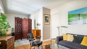 Ein Wohnzimmer mit einer Couch, Sesseln, einem Couchtisch, einem Holzschrank, einem dekorativen Raumteiler und einem Bild an der Wand.