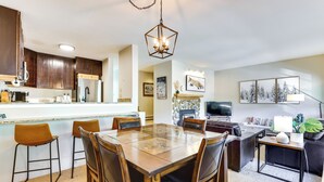 A modern kitchen with dark wood cabinets, a central island, and a dining area with a large wooden table and chairs. - East Vail Condo w/ Pool, Hot Tub, & Free Bus Stop (Vail)