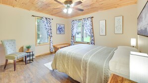 A bedroom with a bed, a chair, a small table with a plant, and a ceiling fan. - Cozy Cable Cabin Rental - Pet Friendly! (Cable)