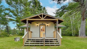 A wooden cabin with a porch, a door, and two wall-mounted lights. - Cozy Cable Cabin Rental - Pet Friendly! (Cable)