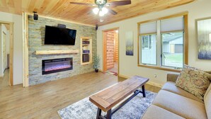 A living room with a stone fireplace, wooden ceiling, and a large window. - Cozy Cable Cabin Rental - Pet Friendly! (Cable)