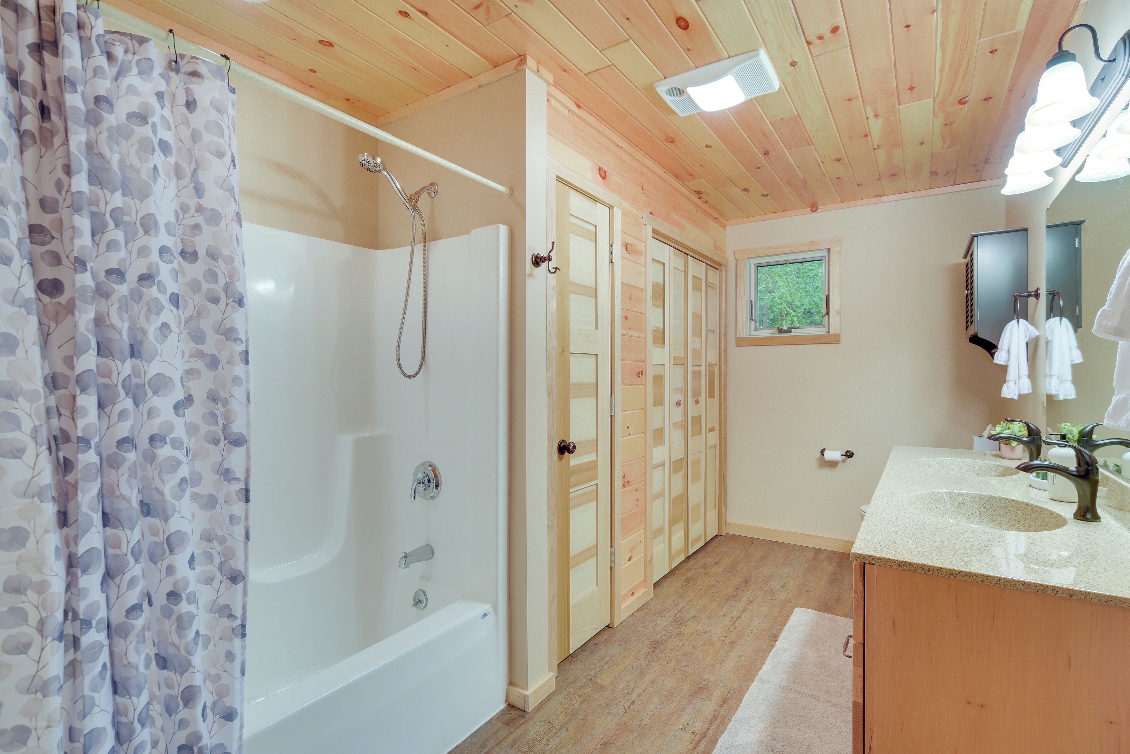 Un baño con bañera, ducha, puertas de madera, un lavabo y un espejo.