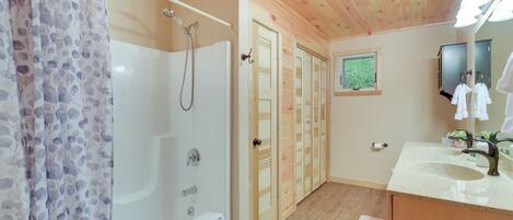 A bathroom with a bathtub, shower, wooden doors, a sink, and a mirror.