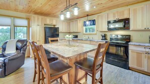 A modern kitchen with wooden cabinets, a granite countertop, a central island with chairs, a black oven, and a microwave. - Cozy Cable Cabin Rental - Pet Friendly! (Cable)