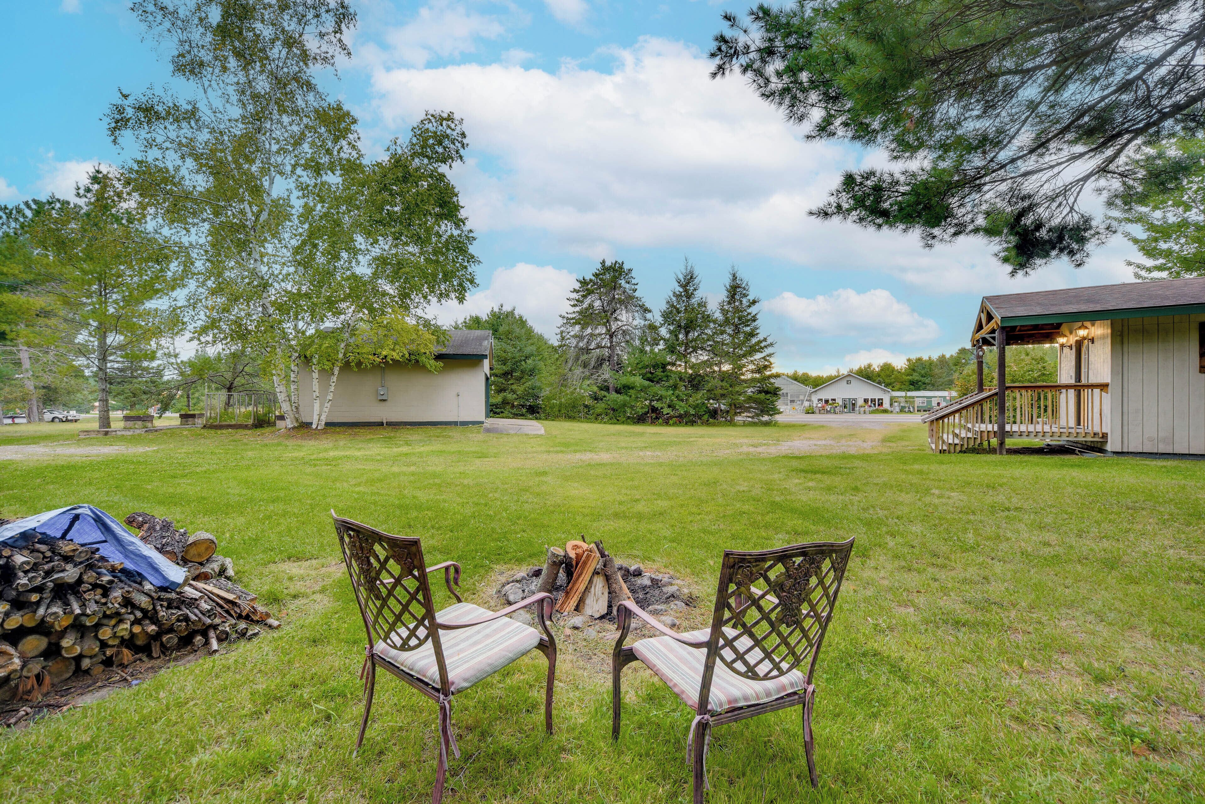 A backyard with two chairs facing a fire pit, surrounded by a grassy lawn and trees.