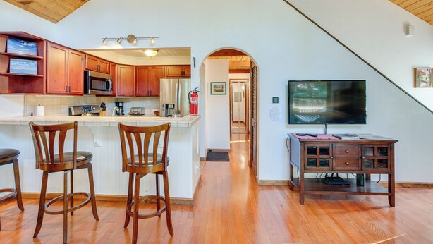 A kitchen with wooden cabinets, a microwave, and a large island with bar stools. There is a television on a wooden stand and a framed picture on the wall. - Hike, Boat & Ski: South Lake Tahoe Home (South Lake Tahoe)