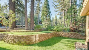 A landscaped yard with a stone retaining wall, a grassy lawn, and tall pine trees. - Hike, Boat & Ski: South Lake Tahoe Home (South Lake Tahoe)