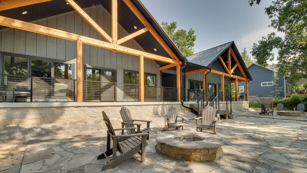 A building with a covered patio area featuring Adirondack chairs, a stone fire pit, and a staircase leading to an upper level. - Riverfront Salesville Cabin Rental w/ Shared Dock! (Mountain Home)